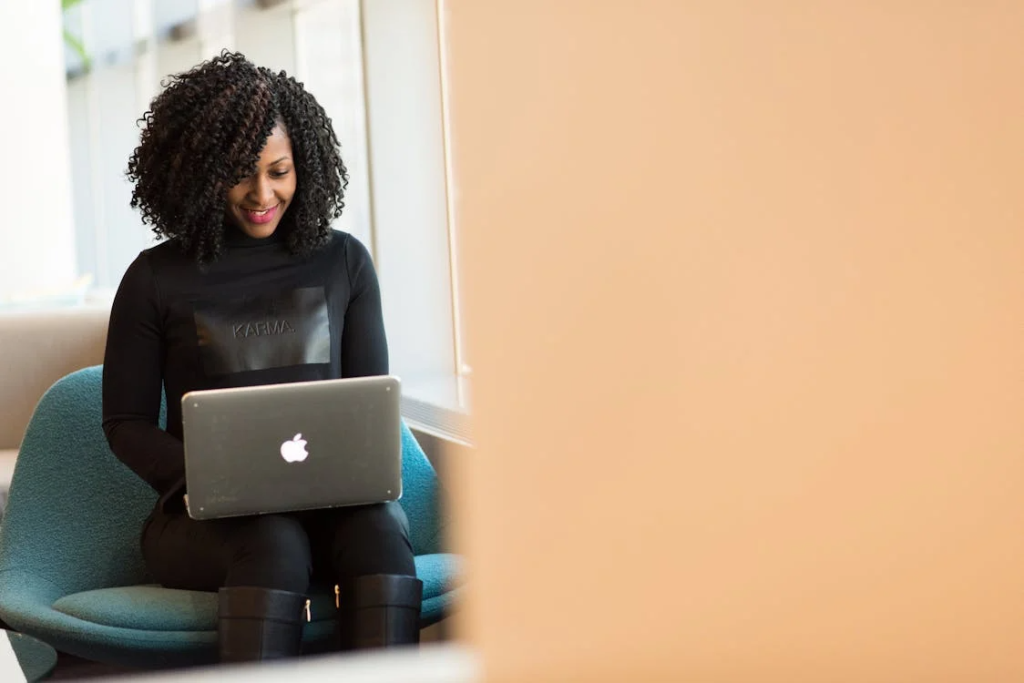 Woman smiling while using a MacBook on a blue sofa, representing positive email marketing results