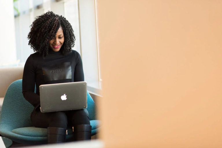Woman smiling while using a MacBook on a blue sofa, representing positive email marketing results